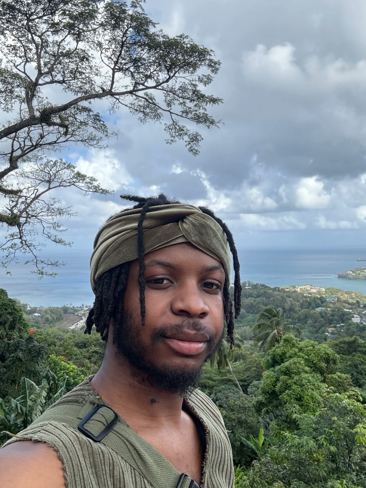 Cyrus portrait with green headwrap against lush hills and sea